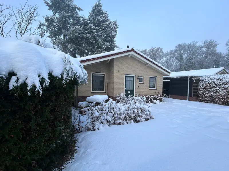 De voorkant van huisje 3 in de winter, met sneeuw op de oprit en de haag.